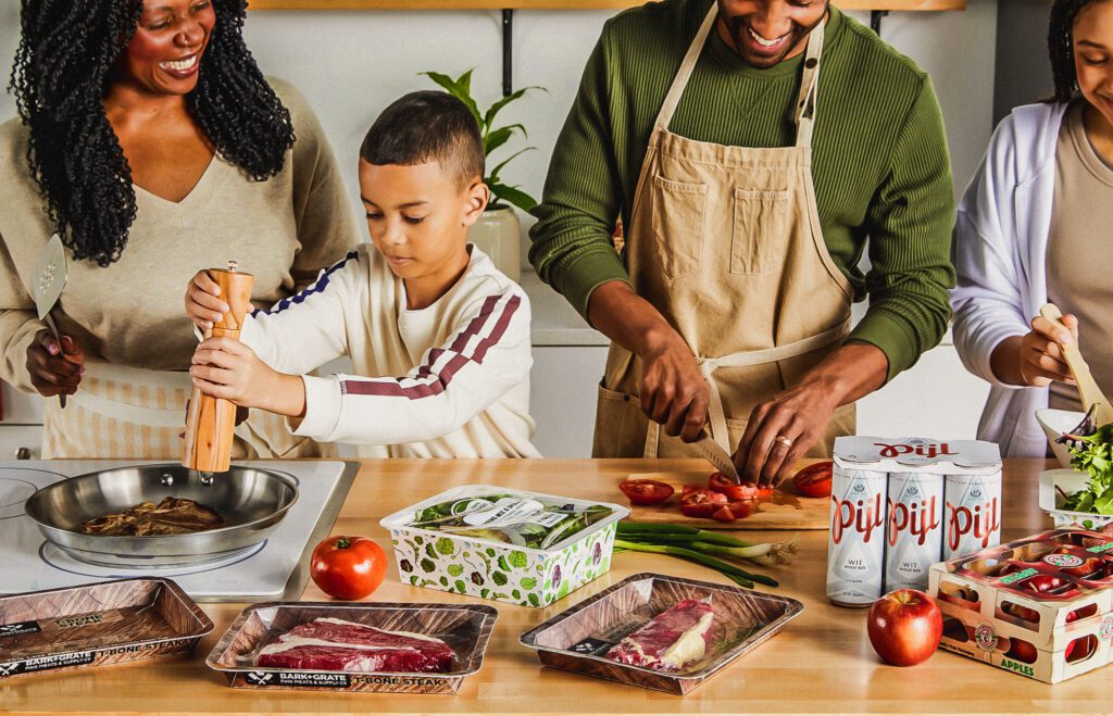 A family of four is cooking, using various Graphic Packaging's products, including PaperSeal tray, ProducePack, and more.