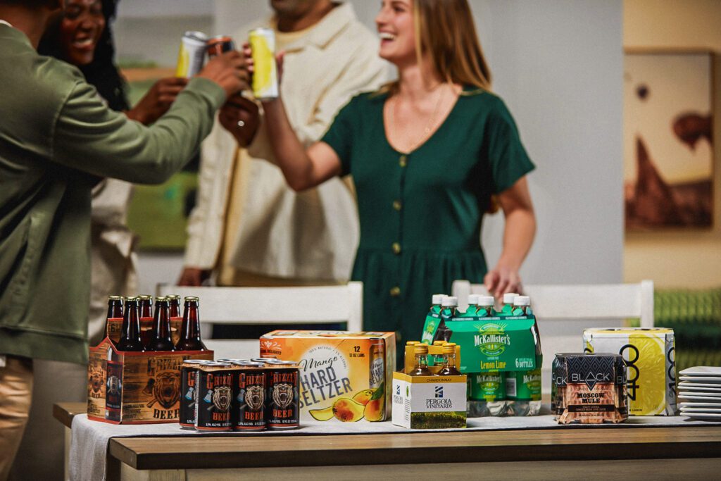 A view showcasing beverage multipacks, including basket carriers, fully enclosed, and clip multipacks, while a group of friends are cheering