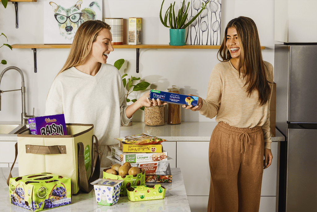 Two women loading groceries from the counter to the fridge