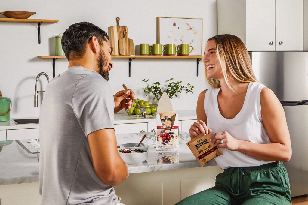 A couple enjoying breakfast at the kitchen island while holding an instant oatmeal pouch