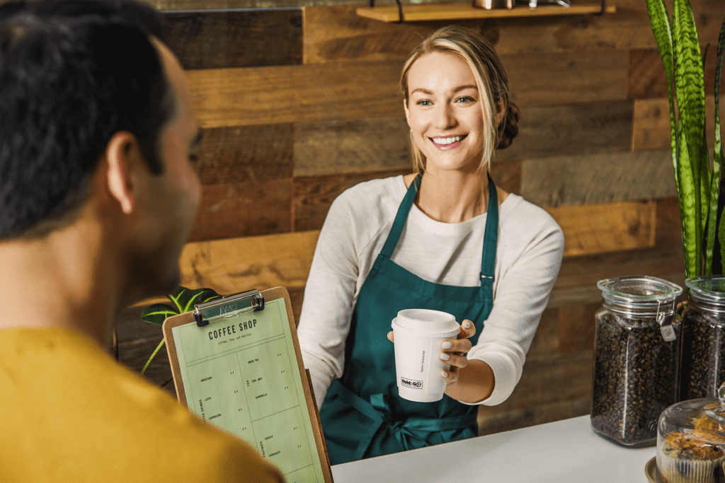 A barista handing a Hold&Go hot cup drink to a customer
