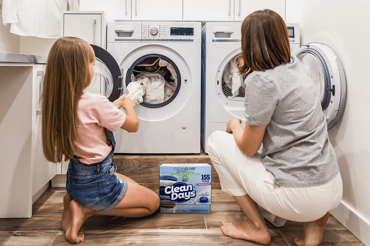 Mother and child putting laundry in a washing machine with the CleanClose child-resistant laundry detergent pod packaging in the foreground.