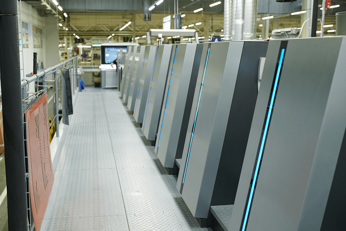 A person tosses a white paper cup into a colorful paper recycling bin outdoors.