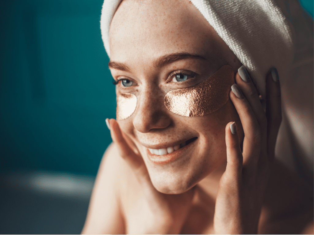 Freckled woman applying golden patches under eyes touching face with hands. Natural beauty. Skin care. Rejuvenation treatment. Eye care.