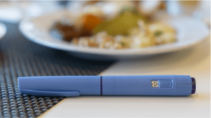 An Ozempic pen on a napkin next to a plate of food